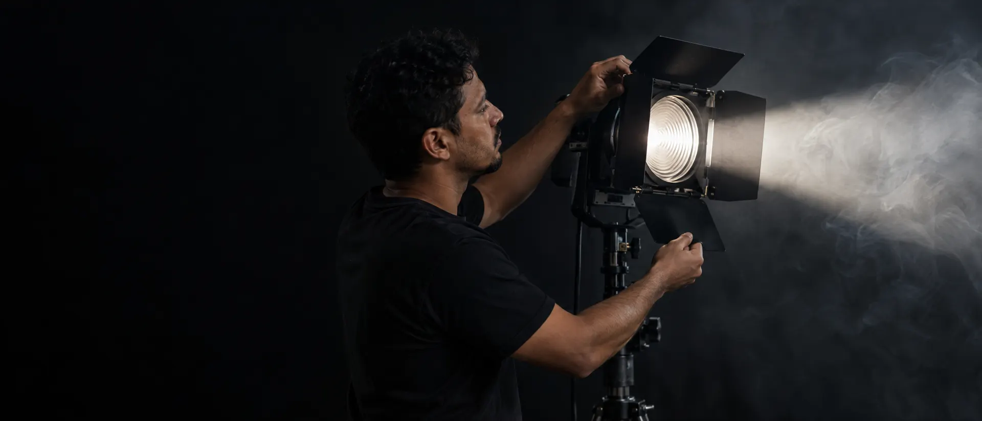Técnico ajustando as abas de uma bandeira num ponto de luz com lente Fresnel, com o feixe atravessando fumaça